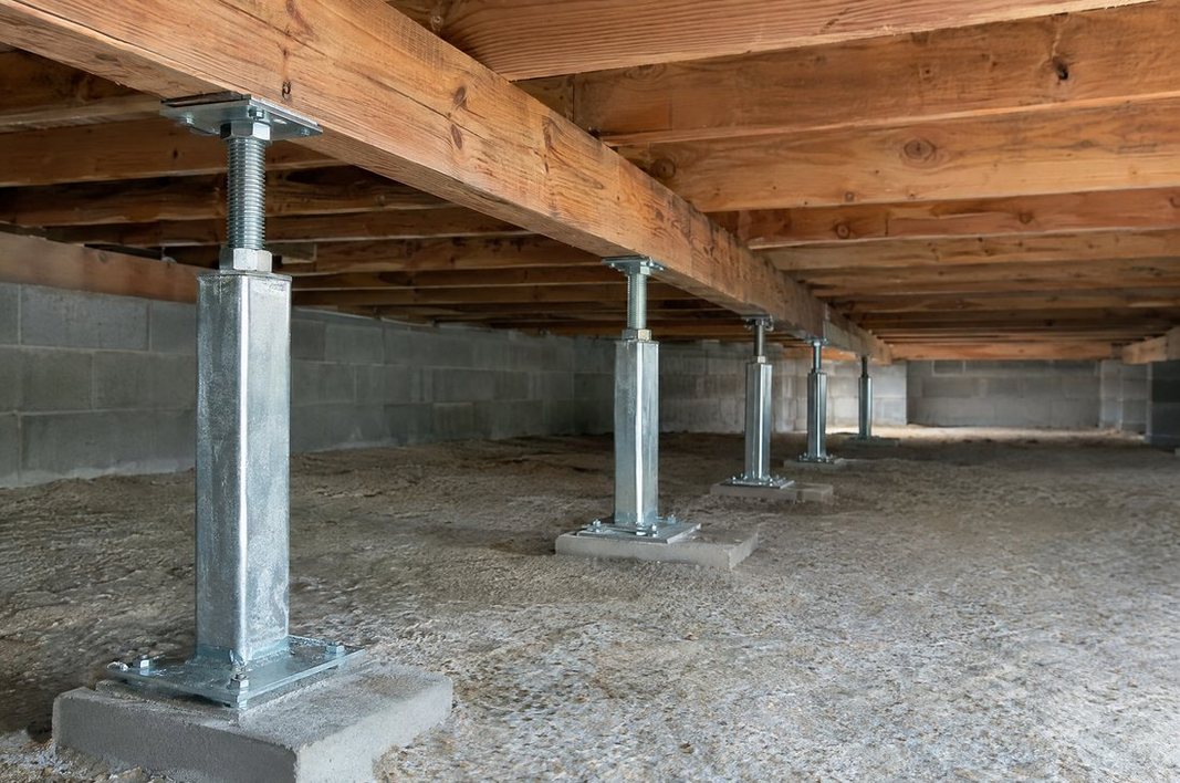 Steel support jack bracing a repaired floor beam in a crawl space